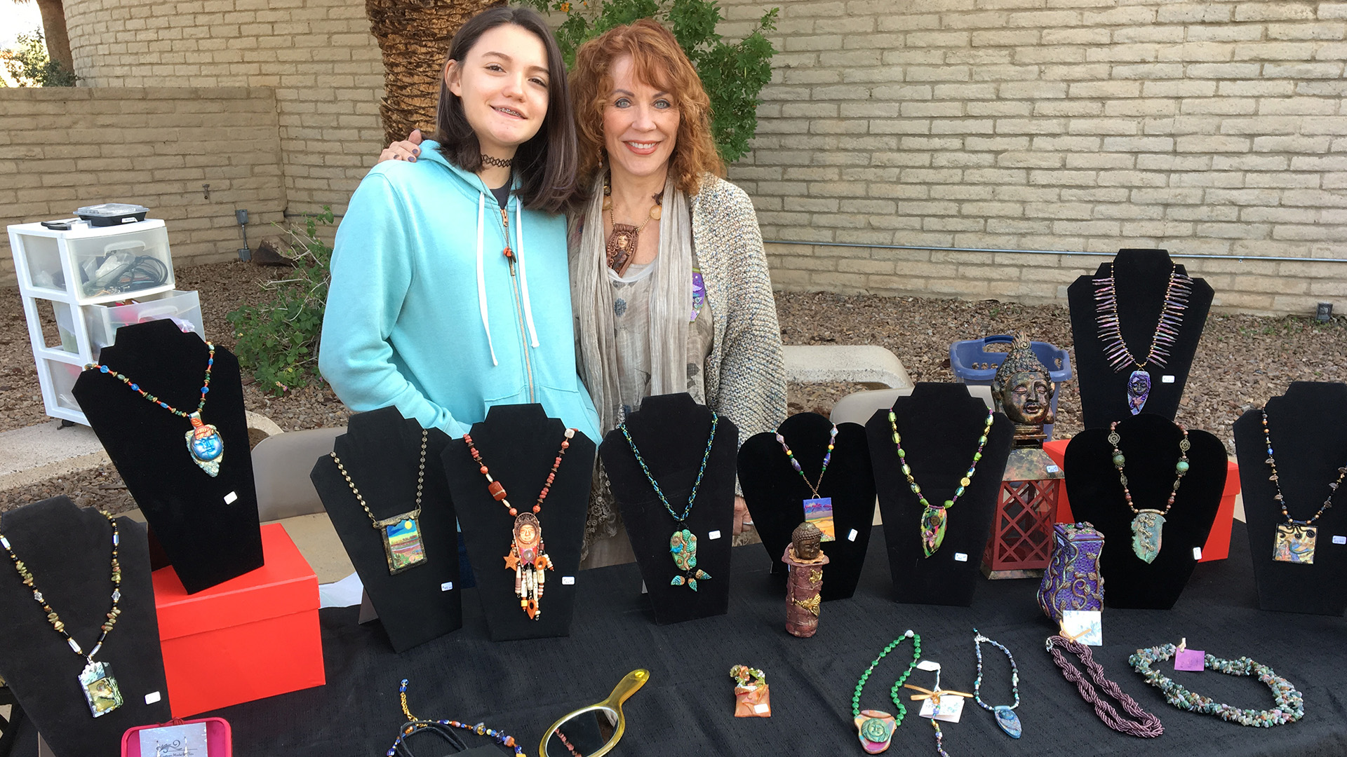 Smiling adult and teen at outside table with handmade jewelry - craft fair