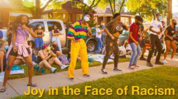 Protesters in Chicago dancing on a sidewalk in bright clothing | "Joy in the Face of Racism" overlaid in gold text