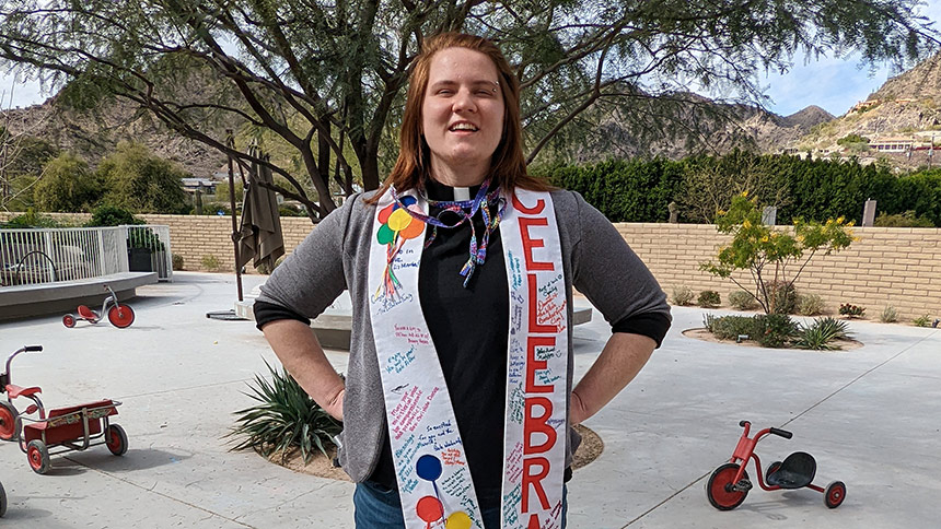 Rev. Sky Williams-Tao standing on patio wearing "CELEBRATE" stole signed by UUCP members