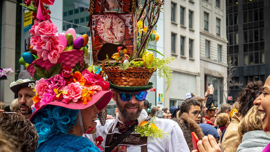 Smiling people wearing elaborte hats gathered in a city street