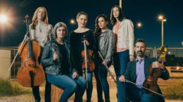 Group of classical musicians in parking lot at night standing in casual clothes, holding their instruments