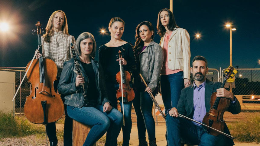 Group of classical musicians in parking lot at night standing in casual clothes, holding their instruments