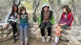 A group of kids sitting on a stone wall while out hiking.