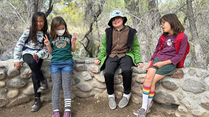 A group of kids sitting on a stone wall while out hiking.