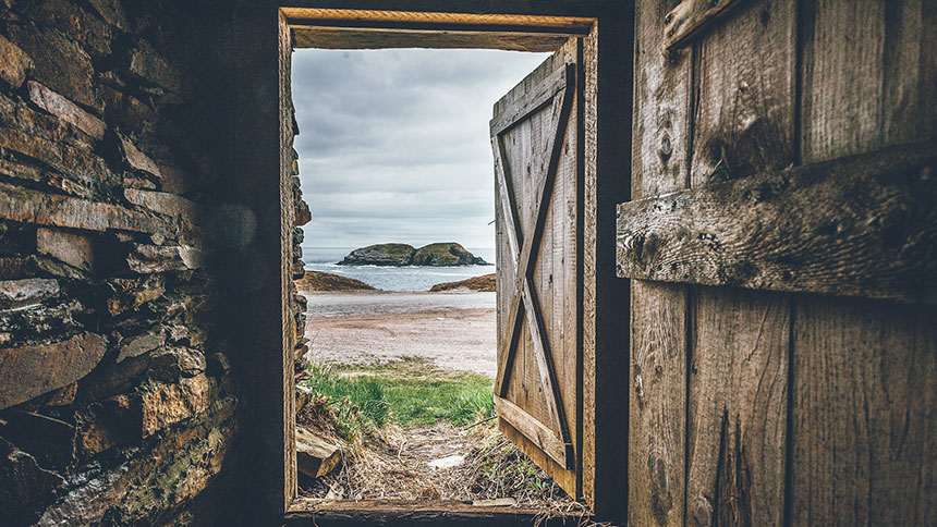 A picture of an open door looking out on to a beach with water and an island in the background.