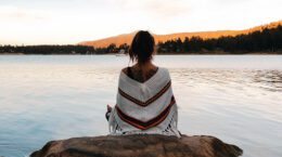 Woman sits near the water on a rock