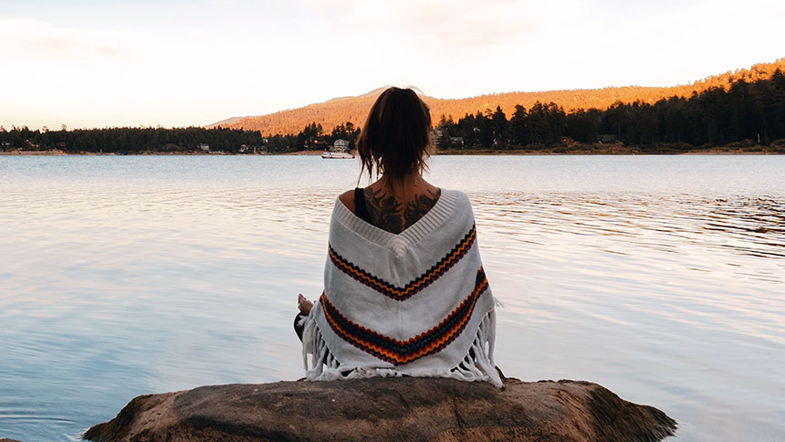 Woman sits near the water on a rock