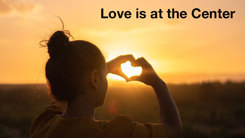 A silhouette of a woman watching a sunset making a heartshape with her hands.