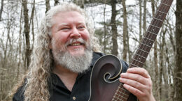 Joe Jencks holding a guitar in a forest.