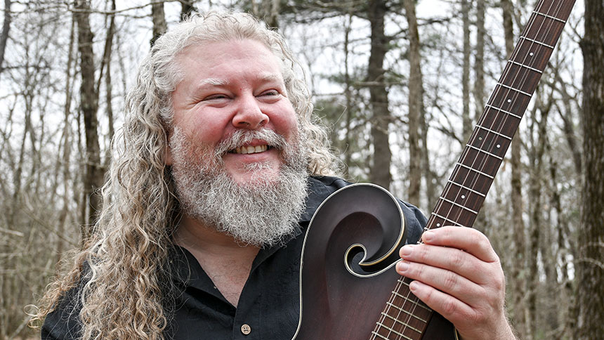 Joe Jencks holding a guitar in a forest.