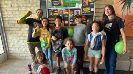 A group of Navigator kids with Jezz and a board of posters behind them.