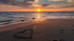 A heart drawn in the sand on a sunset beach.