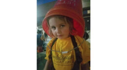 A picture of a kid wearing a yellow t-shirt that says revolutionary education, and has a home depot bucket on her head.